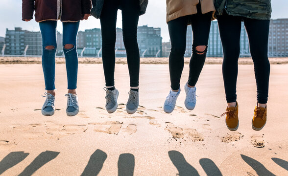 Legs of four friends jumping in the air on the beach