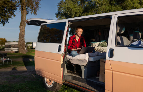 Woman works on a laptop inside a campervan at a sunny campsite