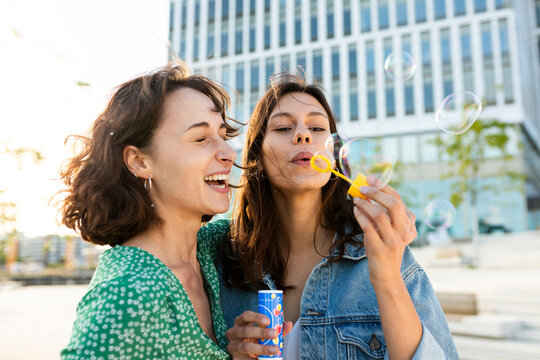Female friends blow soap bubbles and laugh outdoors in the city
