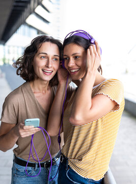 A woman and her friend listen to music on a smartphone outdoors