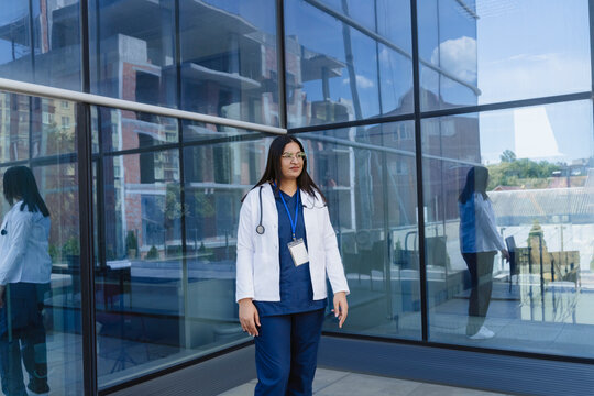A woman doctor in a lab coat enjoys a pause outside the hospital