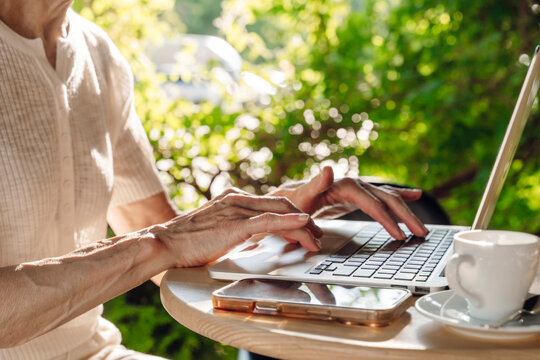 Woman typing on laptop at outdoor cafe table with coffee