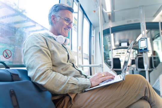 Smiling man works on laptop during tram commute in Barcelona