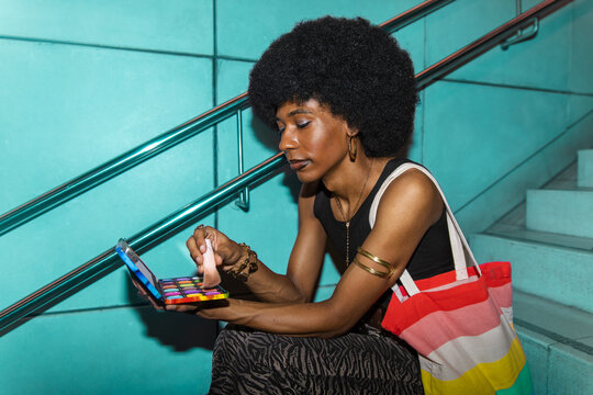 A gender fluid male applies makeup on stairs in a subway station