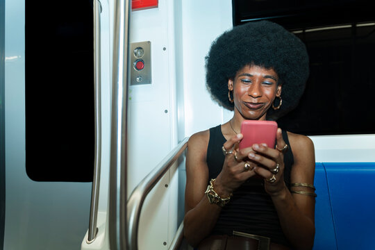 Smiling queer passenger uses smartphone on subway car in Barcelona