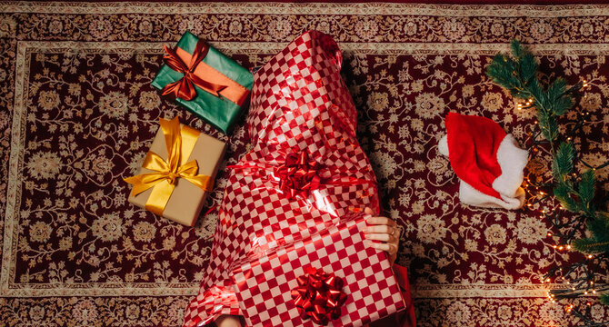 Woman wrapped in red holiday paper lies on carpet with a gift