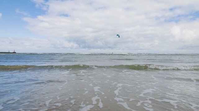 Waves washing ashore on a sandy beach with kitesurfers