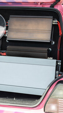 Custom car audio system installation with multiple power amplifiers in vehicle trunk. Automotive tuning showcase featuring intricate wiring, electronic components, vertical composition.