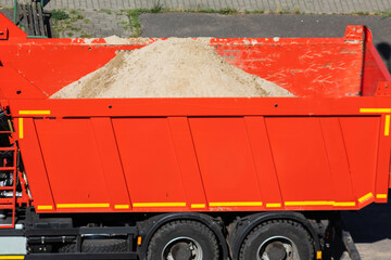 Red dump truck side view with sand material, heavy construction vehicle transporting aggregate for building projects, industrial transport equipment on job site © HENADZY