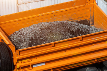 Bright orange dump truck bed loaded with fresh crushed stone for construction, material transport vehicle carrying aggregate for building project during day © HENADZY