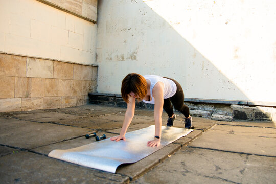 Young Fit Woman Doing Plank Exercise on Fitness Mat Outdoors in Urban Setting