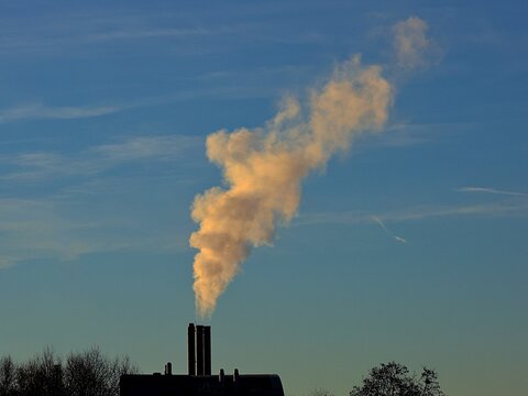 Vue rapproch&eacute;e d'une chemin&eacute;e de laquelle jaillit une &eacute;paisse fum&eacute;e blanche, avec un ciel bleu en arri&egrave;re plan. Symbole de la pollution atmosph&eacute;rique. 