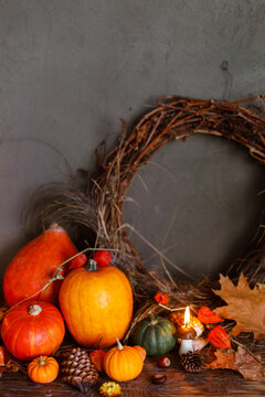 Autumn still life. Colorful pumpkins, autumn leaves, acorns, stylish wreath and candle on rustic wooden table on moody dark background. Happy Thanksgiving and harvest. Fall season greeting card