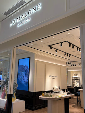 A Jo Malone store in a shopping mall displays elegant fragrance products on a central table. Soft lighting highlights the clean, modern design with white walls and minimal decor.