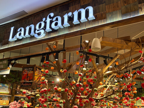 A store display featuring bright decorations with a tree adorned with colorful ornaments. The store name, Langfarm, is prominently illuminated above the scene. The background features warm wooden text