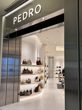 A modern retail store entrance labeled 'PEDRO.' The interior showcases stylish handbags on display shelves. The clean design features bright lighting and a minimalist aesthetic.
