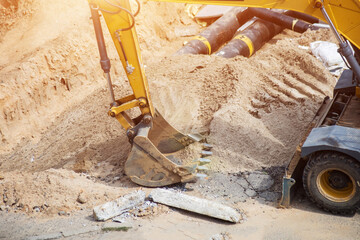 Yellow hydraulic excavator bucket digging earth and sand from a large construction trench. Earthwork activity on a building site showing heavy machinery in action during day, copy space © HENADZY