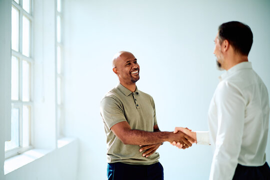 Two diverse businessmen shaking hands, smiling, and celebrating a partnership or successful deal in a bright office