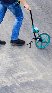 Person walking on asphalt surface using road curvimeter for measurement of distance, surveying for construction or infrastructure project, outdoor activity, work scene vertical photo