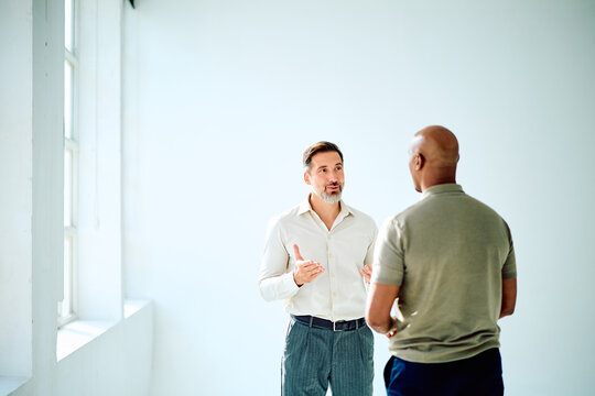 Two diverse businessmen standing, discussing ideas and collaborating in a bright, modern office space