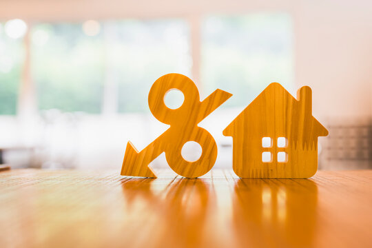 Mortgage rate cut and property loan discount concept with wooden downward percent arrow beside house model on table for lower housing interest, refinancing savings and home buying promotion.