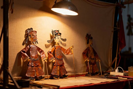 Traditional shadow puppets displayed on a stage under warm lighting, featuring detailed costumes and facial expressions.