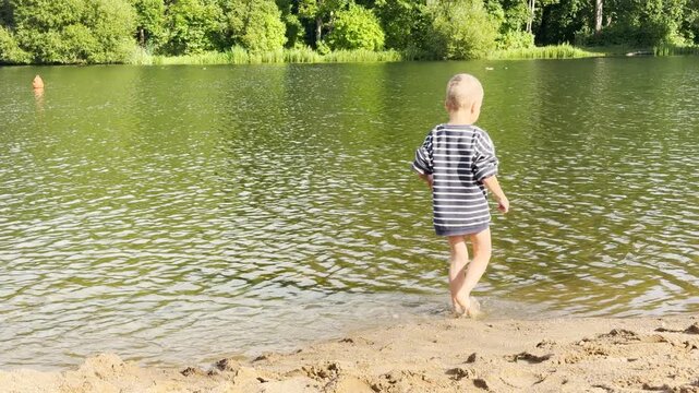 A joyful young boy wades and splashes through the water with pure happiness. He plays along the sandy shore at Kolonistsky Pond Beach in Pushkin, Saint Petersburg.