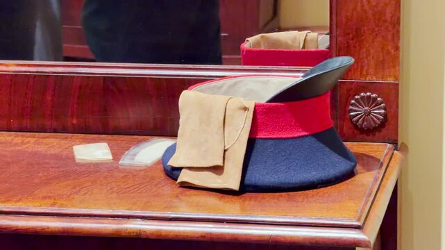 A student cap and gloves rest on a polished wooden table inside the historic Lyceum in Pushkin, Saint Petersburg. The still display evokes a quiet, nostalgic feeling of wonder.