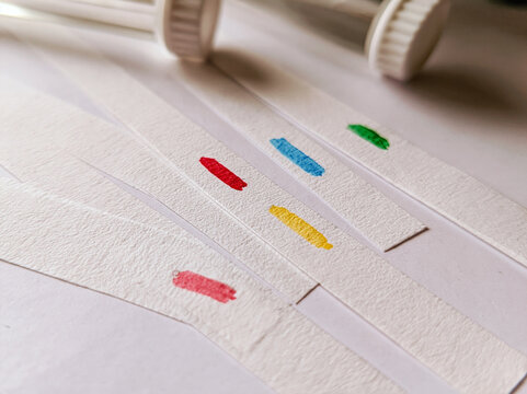 Colorful ink marks on strips of paper, possibly for testing or crafting, with capped tubes in the background