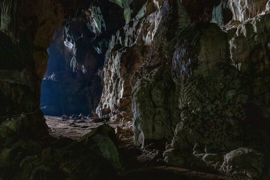 Dark interior of a natural limestone cave showing illuminated stalactite and stalagmite rock formations.
