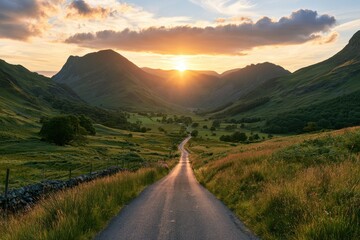 Obraz premium A narrow asphalt road winds through green mountain valleys at sunset. It inspires outdoor travel, freedom, and scenic road trip adventures.