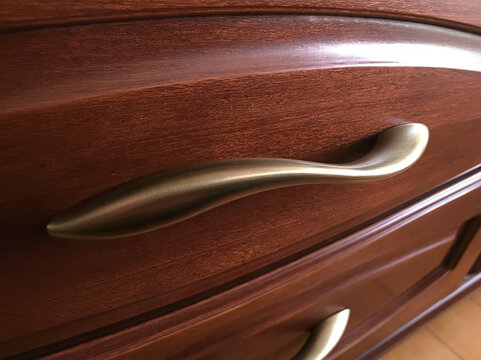 Close-up shot of a brushed brass drawer pull on a dark wood dresser. The detail of the wood grain is visible, adding a touch of elegance and craftsmanship to the furniture.