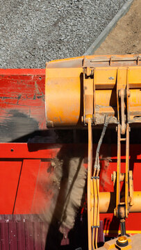 Loader bucket discharging gravel into dump truck bed on construction site from overhead perspective; heavy machinery at work, earthmoving process vertical photo