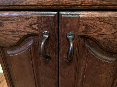 Close up of two antique wooden cabinet doors with ornate curved carvings and dark metal handles