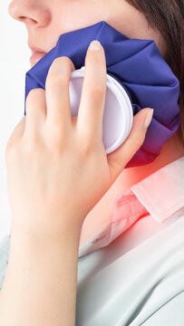 Young adult woman applies cold compress to side of face for pain relief, showing discomfort from inflammation or injury, close up of medical treatment vertical photo
