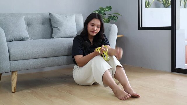 Sad young Asian woman sitting on floor at home feeling distressed with measuring tape showing body insecurity