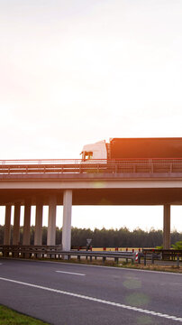 White truck with cargo trailer driving on highway bridge over lower road, modern infrastructure for goods transport and logistics, sun flare sky vertical photo
