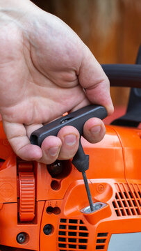 Close-up detail of male hand engaging starter pull cord on bright orange industrial power tool, preparing for operation outdoors during day, vertical photo