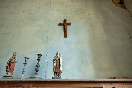 Small religious statues and a wooden crucifix on a cracked plaster wall, Gers, Saint Georges, France