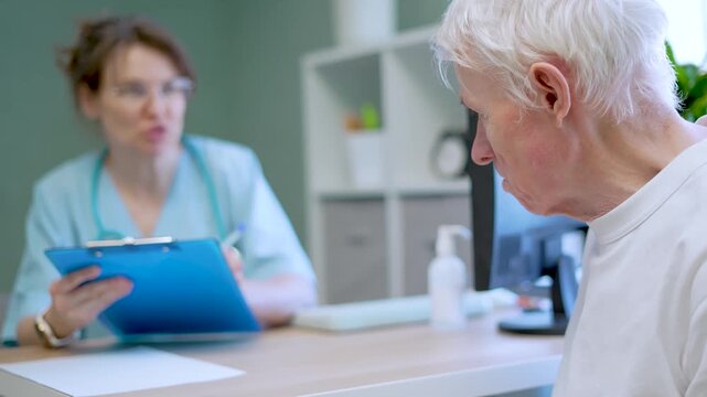 A senior man discusses his health complaints with a female doctor in a clinical setting. The elderly patient listens attentively while the medical professional examines his condition with empathy.