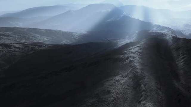 Sunlight breaks through clouds and illuminates mountain ridges in a remote area. The image shows a vast and rugged terrain with shadows and light creating a striking contrast.