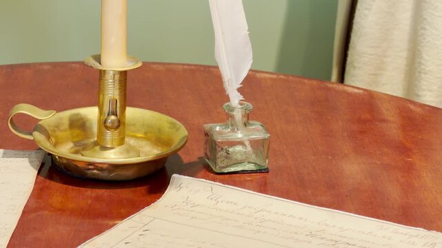 A feather quill in an inkwell and a brass candlestick rest on a wooden desk inside the Lyceum in Pushkin, Saint Petersburg. The scene inspires a quiet feeling of creative wonder.