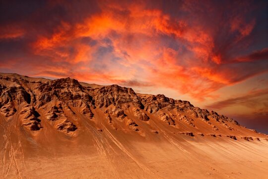 Desert landscape with rugged mountains under a fiery orange and red sky at sunset