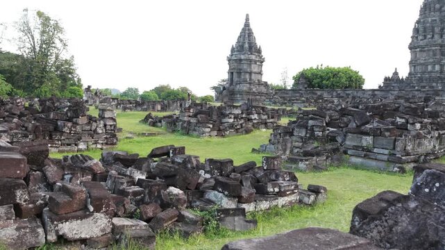 Ancient stone ruins lie scattered across green grass. Weathered towers rise behind fallen walls. Nature slowly reclaims the forgotten temple site. Peaceful atmosphere suggests deep time's passage