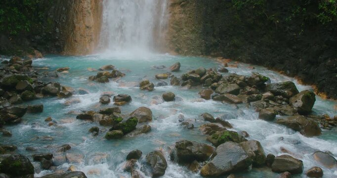Turquoise blue river water rushes over boulders at a waterfalls base in wild nature of Costa Rica