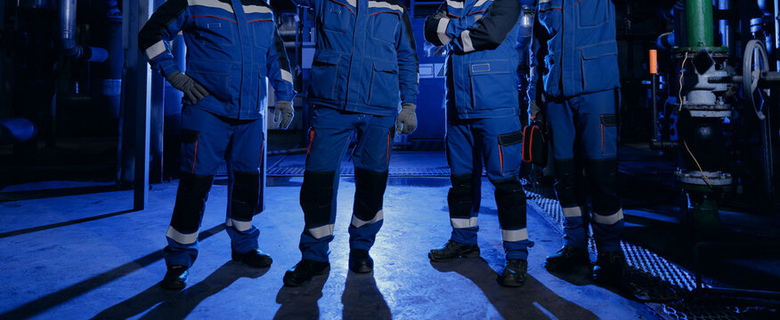 Industrial team of workers standing in plant under blue lighting for safety banner and corporate background emphasizing teamwork and protective workwear