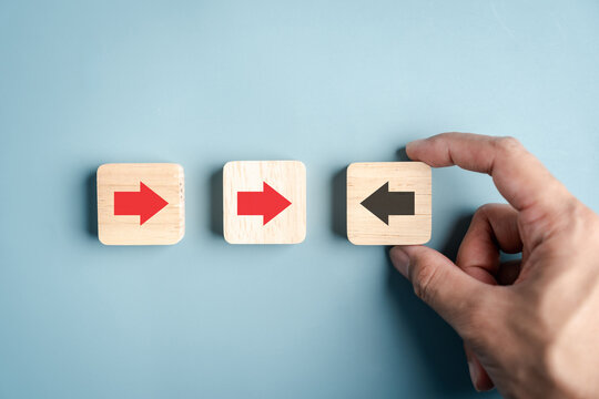 Think different standout opposite arrow direction leadership concept. Hand placing wood block with reverse pointing sign among others.