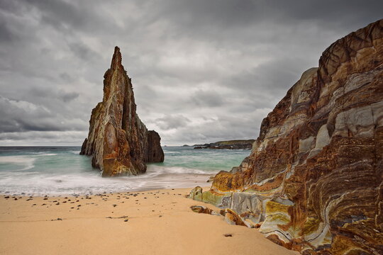 Sharp, central rocky islet midway along Playa de Mexota-A Mixota Beach, at rising tide in a cloudy yet spectacular spring sunrise. Asturias-Spain-014