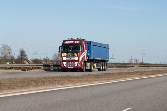 Minsk, Belarus 20.06.23: Red semitrailer truck with blue dump trailer driving on asphalt highway road under clear blue sky day for cargo transport logistics