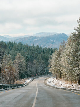 Winter road in snowy mountains. Autumn or wintertime in mountains. Asphalted road through fir tree forest and white snowy mountain peaks in the distance on background. Amazing landscape. Copy space